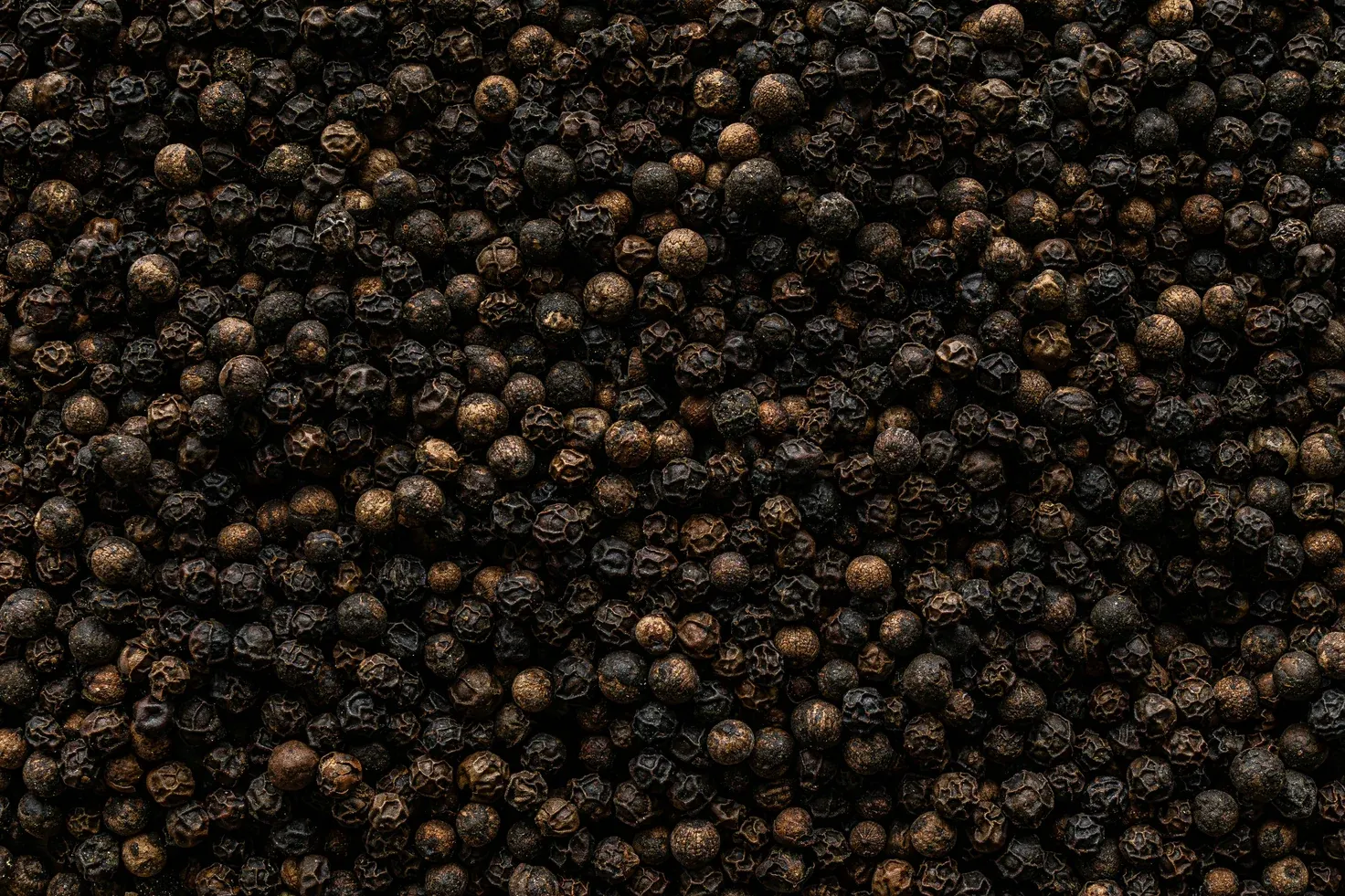 Dried black peppercorns in bulk.