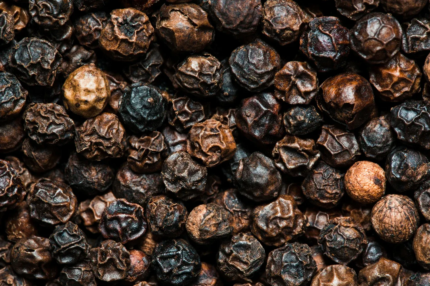 Whole dried black peppercorns, close.